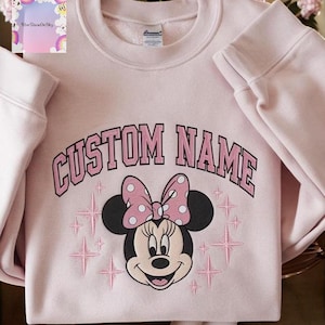 A pink sweatshirt with a Minnie Mouse design and the text "CUSTOM NAME" printed on it.