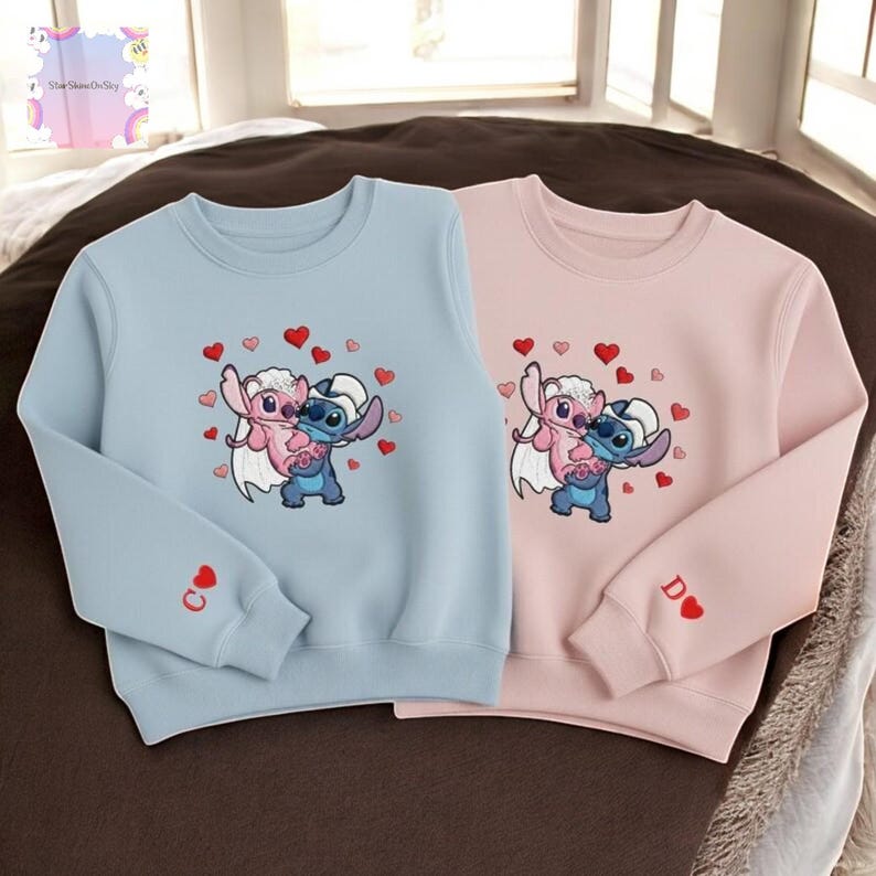 Two children's sweatshirts with a character design, featuring a blue character and a pink character surrounded by hearts.