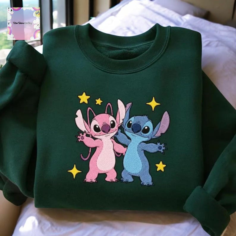 A green sweatshirt with a colorful embroidered design featuring two cartoon characters, one pink and one blue, surrounded by stars and a yellow star.