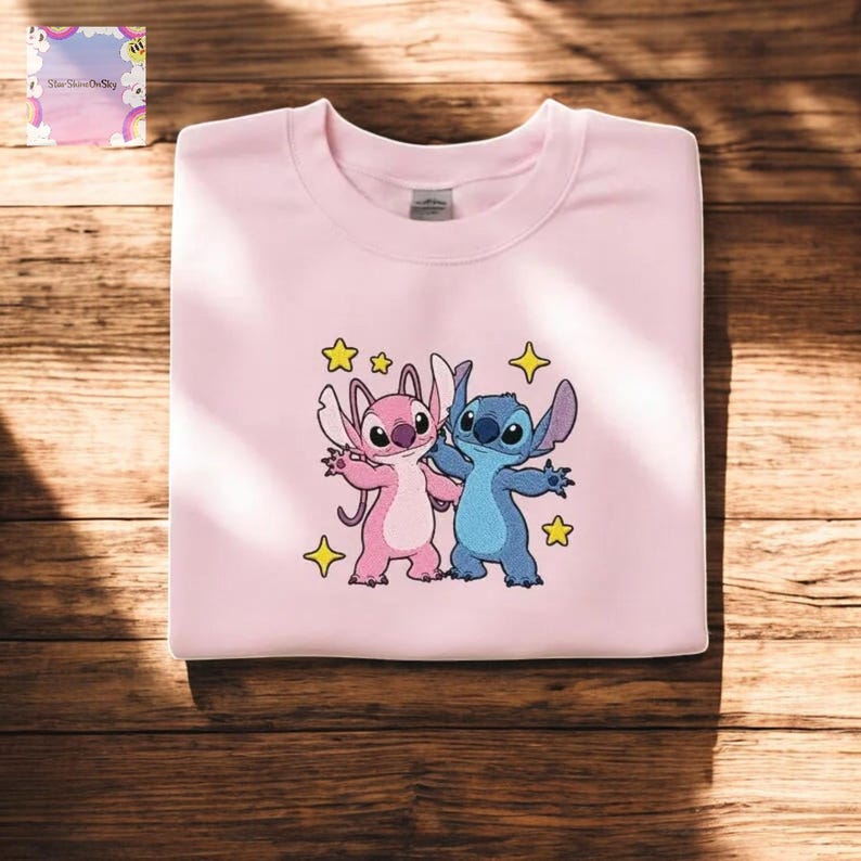 A pink t-shirt with a cartoon image of two cartoon characters, one pink and one blue, surrounded by stars and a yellow star.