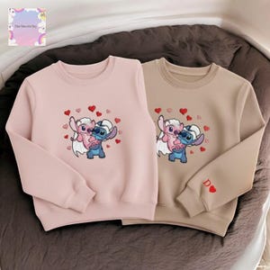 two sweatshirts with a cartoon character design, featuring a pink and blue character with hearts around it.