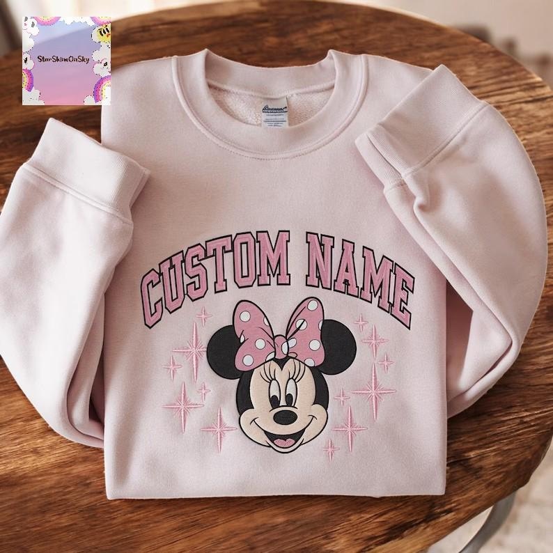 A pink sweatshirt with a Minnie Mouse design and the text "CUSTOM NAME" printed on it.