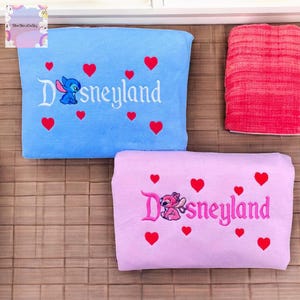 two Disneyland-themed items, including a blue pillow with the word "Disneyland" and a pink pillow with the word "Disneyland", both adorned with red hearts.