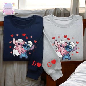 two sweatshirts with a cartoon character design, one in navy blue and the other in gray. The sweatshirts have a heart-shaped motif and the letters 'D' and 'C' on the sleeves.