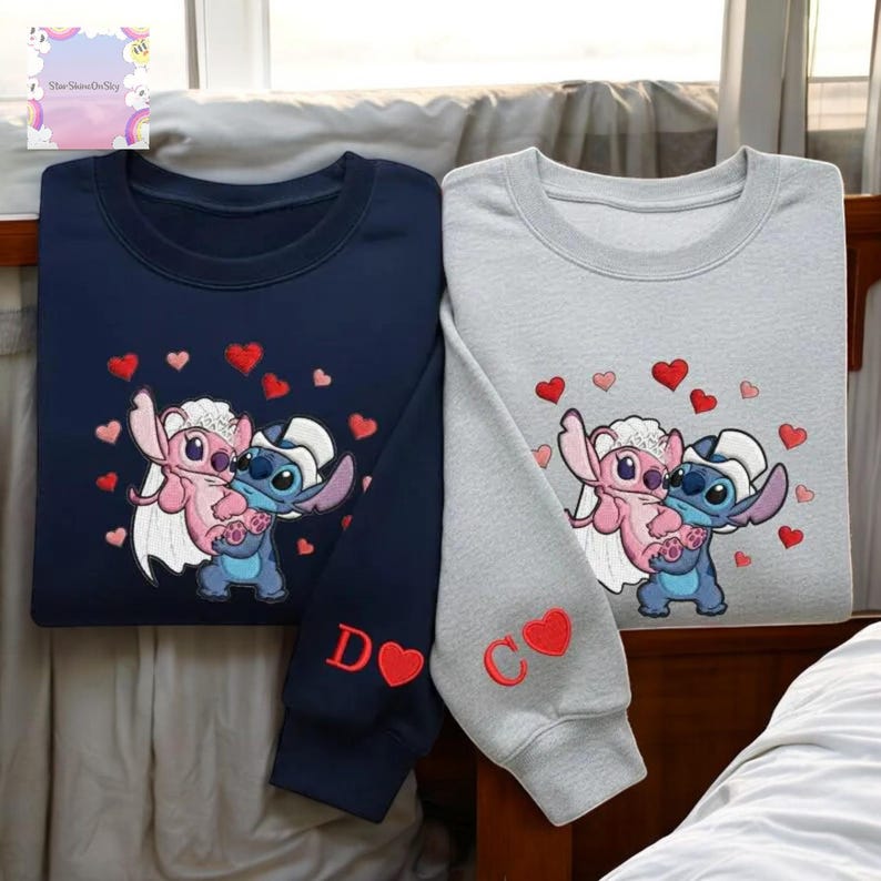 two sweatshirts with a cartoon character design, one in navy blue and the other in gray. The sweatshirts have a heart-shaped motif and the letters 'D' and 'C' on the sleeves.