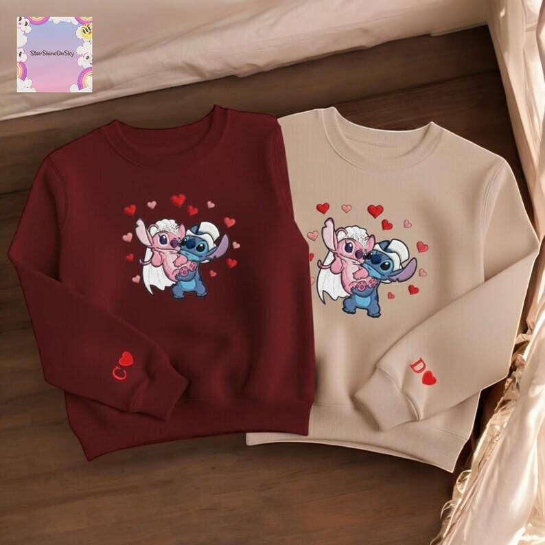 two sweatshirts with the same cartoon character design, featuring a pink and blue character surrounded by hearts.