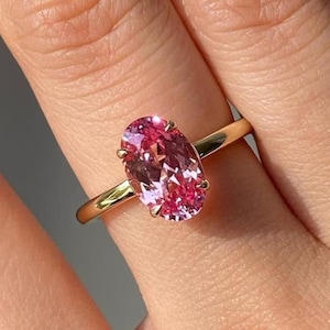 Op de afbeelding: Een gouden ring met een grote, ovale roze edelsteen. De edelsteen is het belangrijkste kenmerk, gezet in een eenvoudige band. De ring wordt op een hand getoond, waarbij de grootte en kleur worden benadrukt. Het ontwerp is elegant.