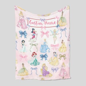 Pu&ograve; includere: Coperta rosa con illustrazioni ad acquerello di principesse e fiocchi. La coperta ha una cornice rettangolare con il testo "Custom Name". Le principesse indossano vari abiti e i fiocchi sono in tonalit&agrave; di blu, rosa e verde.