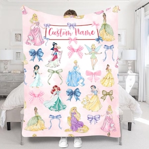 Pu&ograve; includere: Una coperta rosa con illustrazioni di principesse e fiocchi. La coperta ha il testo "Custom Name" in un banner. Le principesse indossano vari abiti e i fiocchi sono in tonalit&agrave; rosa e blu.