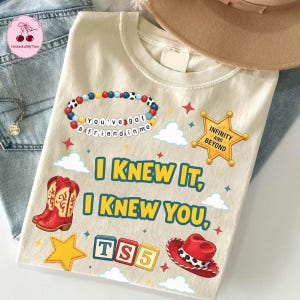 Op de afbeelding: Een cr&egrave;mekleurig t-shirt met een grafische print van een kralenarmband met de tekst You've got a friend in me, een gele sheriffster met Infinity and Beyond, rode cowboylaarzen, een rode hoed, TS5-blokken en de tekst I KNEW IT, I KNEW YOU.