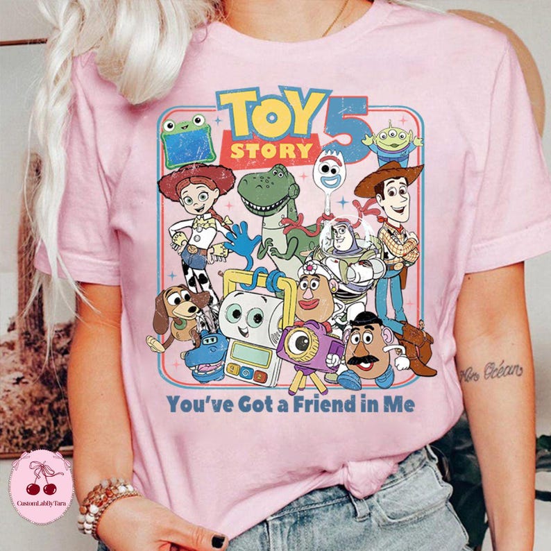 May include: Pink t-shirt featuring a colorful graphic of Toy Story characters, including Woody, Buzz Lightyear, and Rex. The text "TOY STORY 5" is at the top, with "You've Got a Friend in Me" at the bottom.