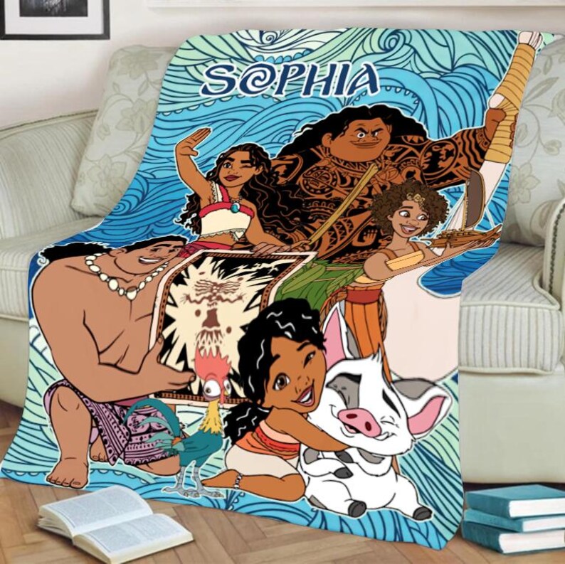 May include: A colorful blanket featuring characters from the animated movie Moana. The blanket has a blue wave pattern background with the name "SOPHIA" in blue script. The characters include Moana, Maui, and Pua the pig.