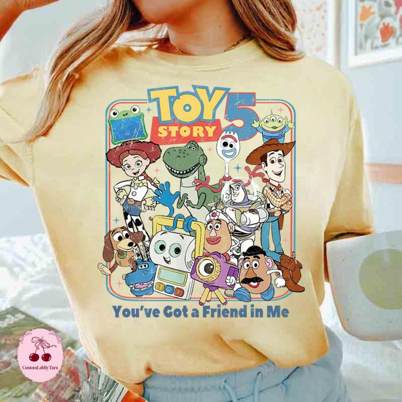 May include: Yellow t-shirt featuring a graphic of characters from the movie "Toy Story." The design includes the text "Toy Story 5" and the phrase "You've Got a Friend in Me." The shirt has a vintage, retro style.