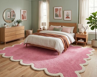 May include: A large, rectangular area rug with a textured, bright pink center and a thick, cream-colored scalloped border. The rug is made of a plush, tufted material and features a distinct wavy edge design that frames the entire perimeter of the piece.