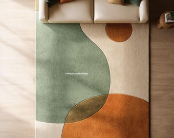 May include: A modern area rug with an abstract design. The rug features large, overlapping shapes in shades of green, orange, and cream. The text "ChhayaCarpetsDesign" is visible on the rug. The rug is placed on a wooden floor, with a cream-colored sofa and pillows in the background.