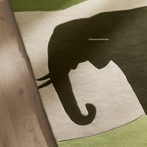 May include: A close-up of a rug featuring a large, dark green elephant silhouette against a light gray background. The rug has green borders and the text "ChhayaCarpetsDesign" is visible.