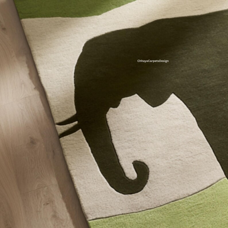 May include: A close-up of a rug featuring a large, dark green elephant silhouette against a light gray background. The rug has green borders and the text "ChhayaCarpetsDesign" is visible.