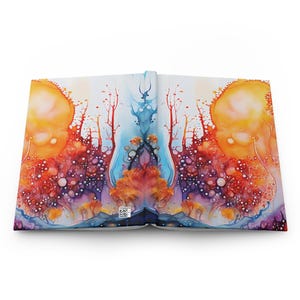 May include: An open hardcover book displaying a symmetrical, abstract watercolor-style illustration across both pages. The artwork features vibrant orange, red, purple, and blue ink-like patterns with tree-like silhouettes and a small QR code at the bottom.