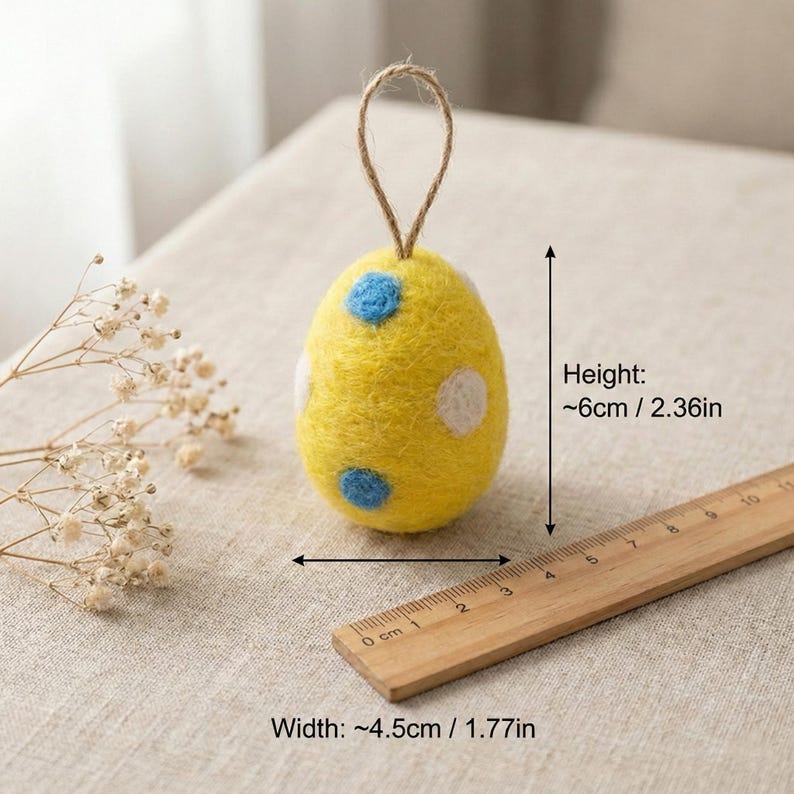 May include: A yellow felt Easter egg ornament with blue and white polka dots. The egg is approximately 2.36 inches tall and 1.77 inches wide, with a jute loop for hanging. A wooden ruler is next to the egg.