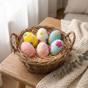 May include: A woven basket filled with six colorful, decorative Easter eggs. The eggs are pastel pink, yellow, white, and blue, with floral and dot designs. The basket sits on a wooden surface, with a neutral-colored blanket in the background.