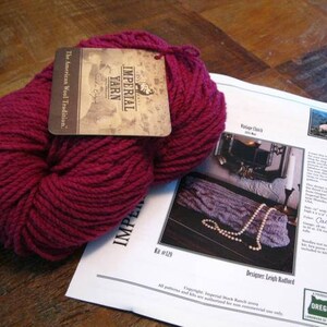 Può includere: Un gomitolo di filato rosa scuro etichettato "Imperial Yarn, The American Wool Tradition". Il filato è su uno sfondo bianco con uno schema per un design "Cactus Blossom".