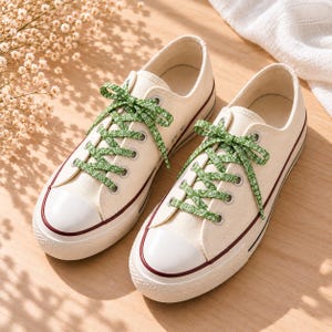Può includere: Un paio di sneakers in tela color bianco sporco con lacci verdi a fantasia paisley bianca. Le scarpe basse presentano punte in gomma bianca, suole in gomma bianca con una sottile striscia bordeaux e occhielli in metallo argentato.