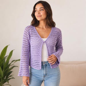 May include: A light purple, open-front crochet cardigan with long sleeves and a V-neck. The cardigan has a delicate, open weave pattern. The sleeves flare slightly at the wrist. The cardigan is worn over a white top and paired with blue jeans.