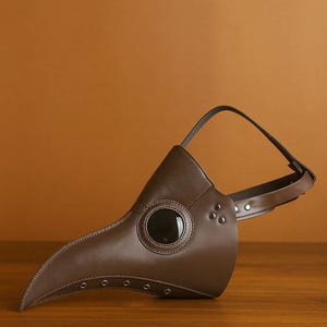Puede incluir: Una m&aacute;scara de m&eacute;dico de la peste de cuero marr&oacute;n con un pico largo y curvado y una lente ocular grande y oscura. La m&aacute;scara tiene una correa para sujetarla a la cabeza y est&aacute; dise&ntilde;ada con remaches y costuras. Accesorio de disfraz hist&oacute;rico.