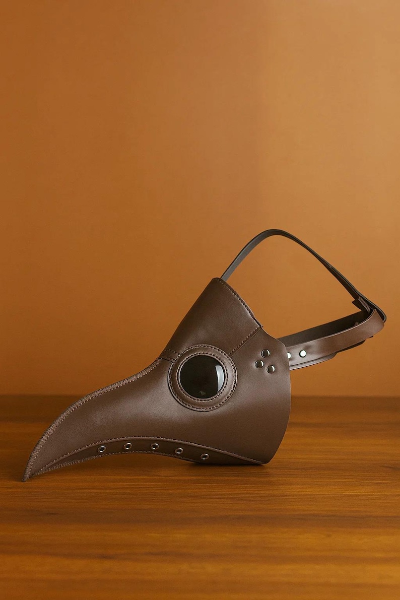 Puede incluir: Una m&aacute;scara de m&eacute;dico de la peste de cuero marr&oacute;n con un pico largo y curvado y una lente ocular grande y oscura. La m&aacute;scara tiene una correa para sujetarla a la cabeza y est&aacute; dise&ntilde;ada con remaches y costuras. Accesorio de disfraz hist&oacute;rico.