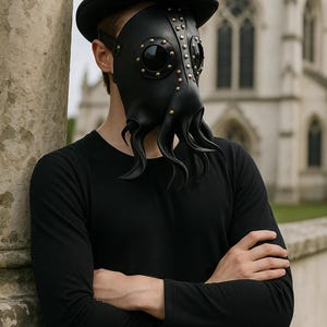 May include: Black leather plague doctor mask with brass rivets and tentacle-like extensions. The mask has large, dark eye lenses and is paired with a black top hat. The person is wearing a black long-sleeve shirt.