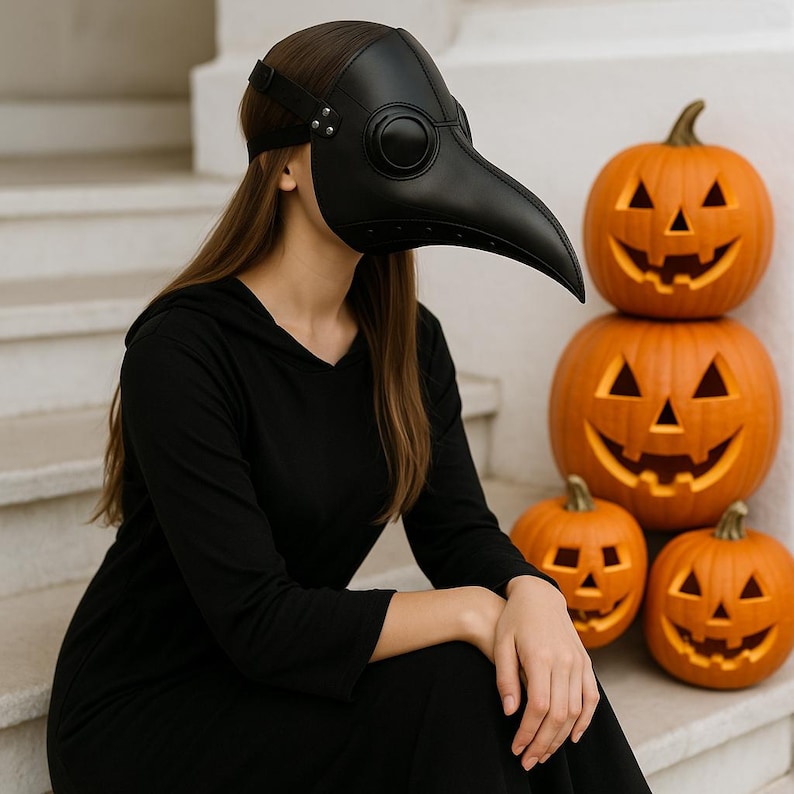 Puede incluir: Una m&aacute;scara negra de m&eacute;dico de la peste con un pico largo, usada por una persona con un vestido negro con capucha. La m&aacute;scara tiene grandes aberturas redondas para los ojos. Calabazas naranjas talladas con caras de jack-o'-lantern apiladas.