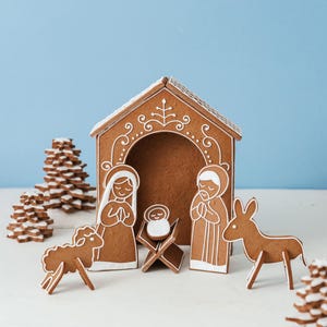 May include: Gingerbread nativity scene with a house, figures of Mary, Joseph, and baby Jesus, a sheep, and a donkey. The gingerbread is decorated with white icing details. Christmas holiday decor.