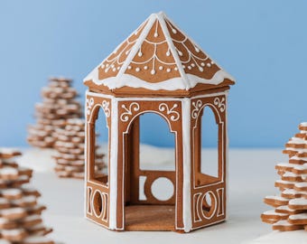 May include: A brown gingerbread gazebo with a hexagonal roof and open arched sides. The structure is decorated with white icing in intricate scrollwork patterns along the roof panels and pillars, featuring a pointed roof and a hollow interior.