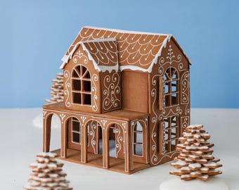 May include: A gingerbread house with brown walls and white icing details, featuring a multi-level structure, arched windows, and a covered porch. The roof is decorated with white scalloped icing patterns, and the house is surrounded by small stacked gingerbread trees.