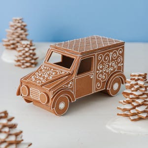 May include: A gingerbread van decorated with white icing swirls on the hood and side panels, featuring a cross-hatched roof pattern. The van is surrounded by several small, stacked star-shaped gingerbread trees topped with white icing.