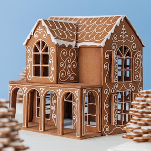 Può includere: Una dettagliata casa di pan di zenzero con dettagli in glassa bianca. La casa presenta più piani, finestre ad arco e un portico. Il tetto e i bordi sono decorati con intricati motivi di glassa. La casa è su uno sfondo azzurro.