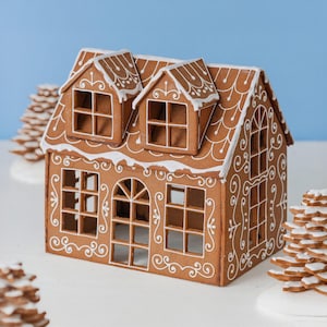 May include: A brown gingerbread house with white icing details, featuring two dormer windows on the roof, a central arched doorway, and multiple square-paned windows. The structure is decorated with white piped scrollwork and roof trim.