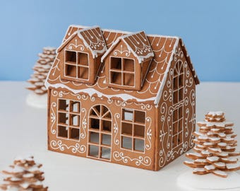 May include: A brown gingerbread house with white icing details, featuring two dormer windows on the roof, a central arched doorway, and multiple square-paned windows. The structure is decorated with white piped scrollwork and roof trim.