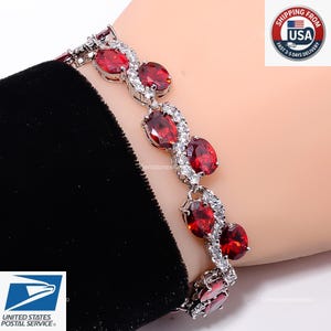 May include: A silver-toned bracelet featuring a series of oval-cut deep red gemstones arranged in a repeating pattern, interspersed with small clear white stones set along the metal links that connect each of the larger red oval gems.