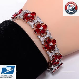 May include: A silver-toned bracelet featuring a series of flower-shaped links. Each flower is composed of four deep red, marquise-cut stones with a small, clear, round stone at the center. The links are connected by small, clear, marquise-cut stones.