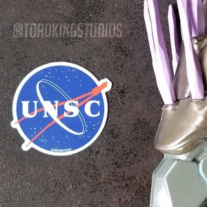 May include: A close-up of a silver and gold toy weapon with purple spikes. The weapon has a detailed design and is a popular collectible for fans of science fiction.