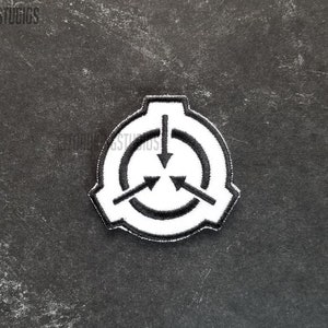 May include: A white and black embroidered patch featuring the SCP Foundation logo. The logo consists of a circle with three downward-pointing arrows and a surrounding border. The patch is on a dark gray textured surface.