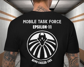 Op de afbeelding: Zwart T-shirt met een witte afbeelding van een negenstaartige vos-logo en de tekst "Mobile Task Force Epsilon-11 Nine-Tailed Fox".