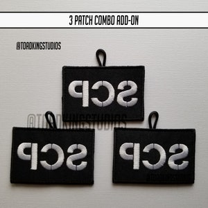 以下が含まれることがあります： 白文字で「SCP」と刺繍された黒いパッチが3つ。各パッチの上部にはループが付いています。「3 PATCH COMBO ADD-ON」と「@TOADKINGSTUDIOS」の文字も表示されています。