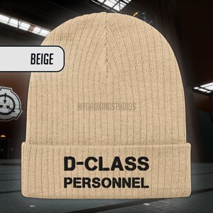 May include: Beige knitted beanie with the text "D-CLASS PERSONNEL" in black.
