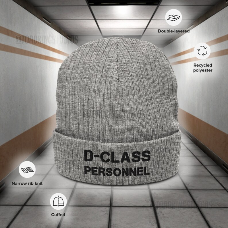 May include: Grey knitted beanie with a black embroidered design that reads "D-CLASS PERSONNEL". The beanie is double-layered, made from recycled polyester, and has a narrow rib knit cuff.