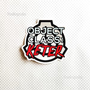 May include: A white sticker with a black border featuring the text "OBJECT CLASS: KETER" in white and red. The sticker has a unique symbol design and is set against a dotted background.