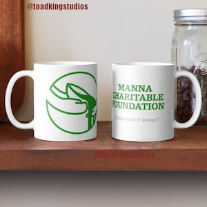 Puede incluir: Dos tazas de cerámica blanca con un logotipo y texto verdes. La taza de la izquierda tiene un logotipo verde de dos manos sosteniendo un tazón. La taza de la derecha tiene el texto "MANNA CHARITABLE FOUNDATION" y el texto "Relief where it belongs."