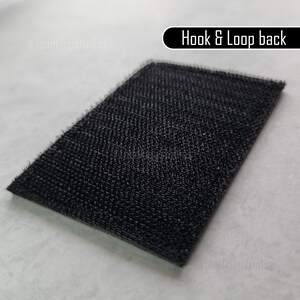 K&ouml;nnte beinhalten: Ein rechteckiger schwarzer Klettverschluss mit strukturierter Oberfl&auml;che. Der Text "Hook & Loop back" ist in Wei&szlig; auf schwarzem Hintergrund dargestellt.