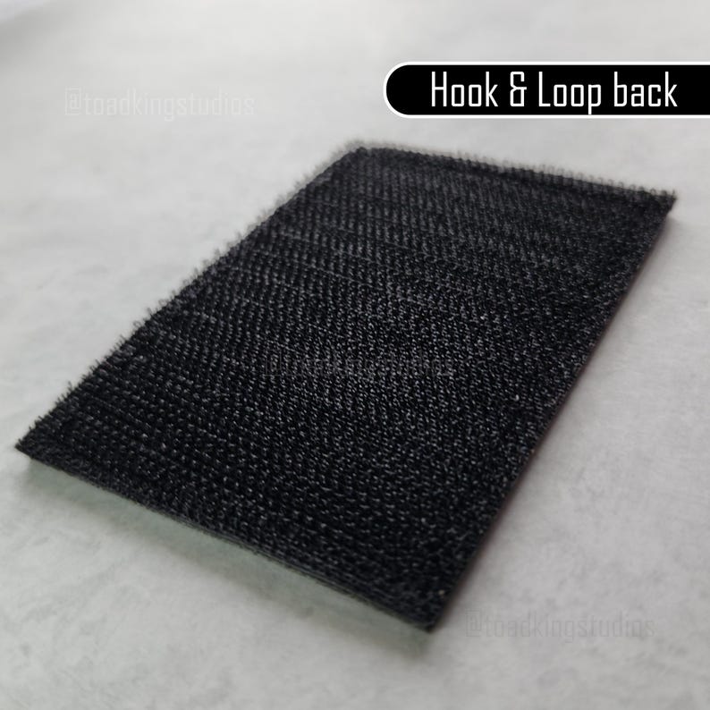K&ouml;nnte beinhalten: Ein rechteckiger schwarzer Klettverschluss mit strukturierter Oberfl&auml;che. Der Text "Hook & Loop back" ist in Wei&szlig; auf schwarzem Hintergrund dargestellt.